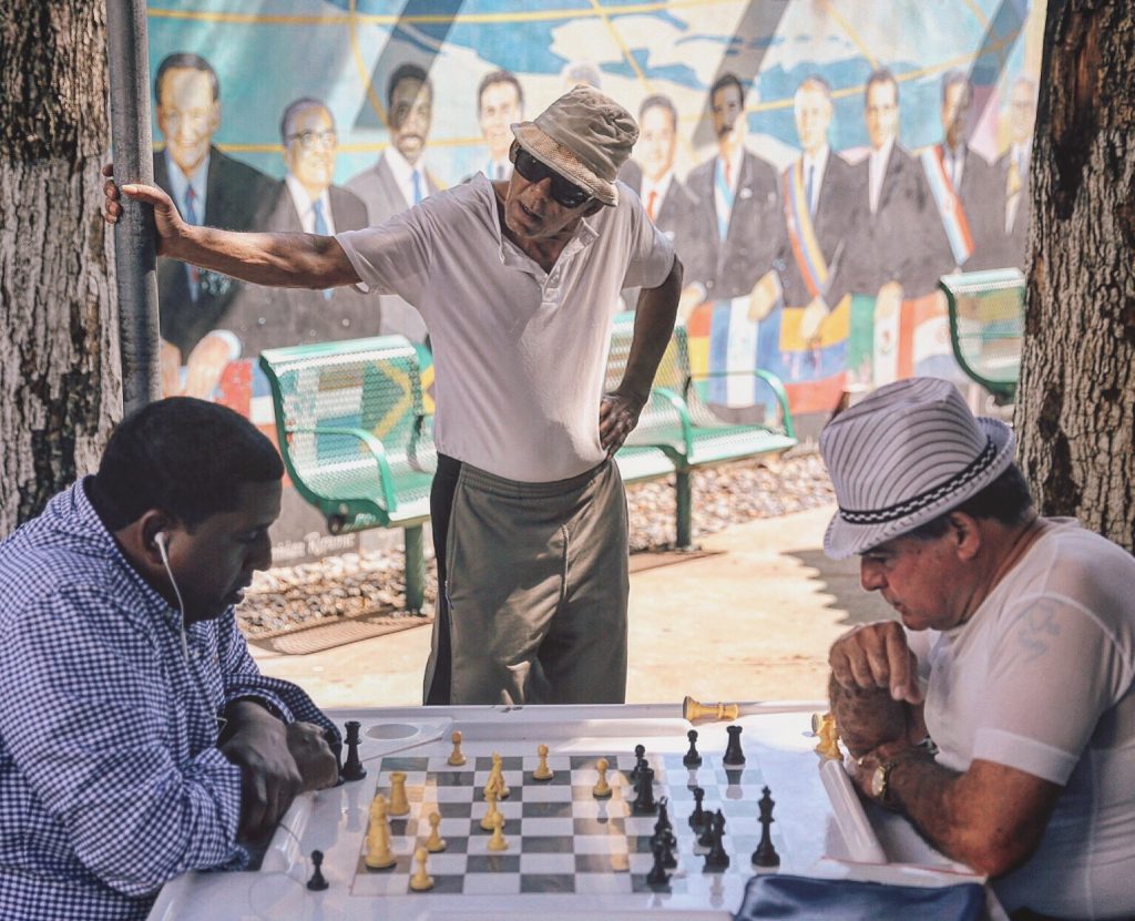 Gentlemen playing chess on a street board while an older man spectates in Little Havana in Miami, Florida.