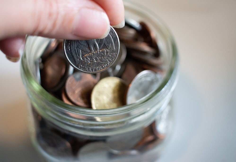 Close up of a change jar where a person is adding a quarter.