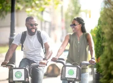 A couple enjoys a bike ride through a small town on a sunny summer day, laughing together.