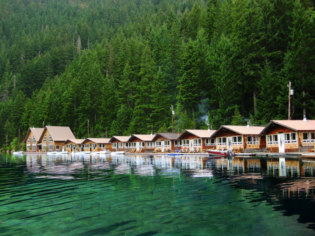 The floating cabins at Ross Lake in Washington sit against a lush green forest and a stunning green lake.