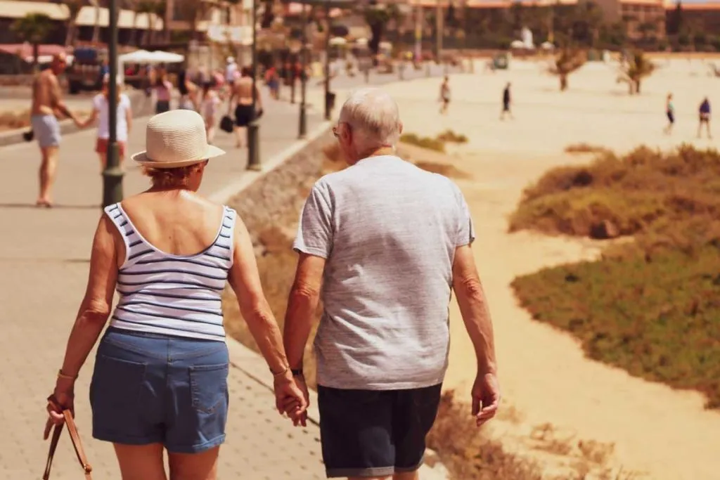 Two senior adults holding hands and walking along the beach, enjoying retirement.
