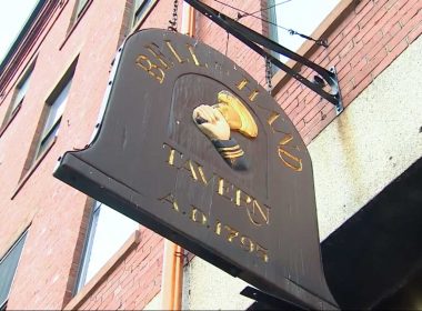 A brown wooden sign hanging outside Bell In Hand Tavern in Boston.